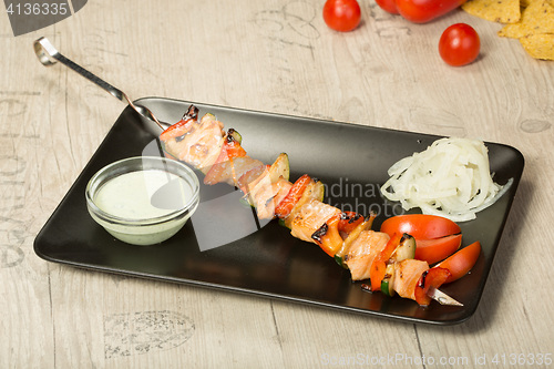 Image of shashlik. kebab skewer, black rectangular plate. sauce and onions