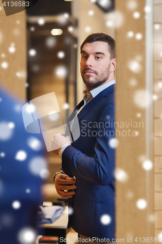 Image of man trying jacket on at mirror in clothing store