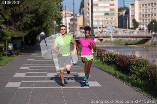 Image of young smiling multiethnic couple jogging in the city
