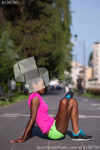 Image of sporty young african american woman stretching outdoors