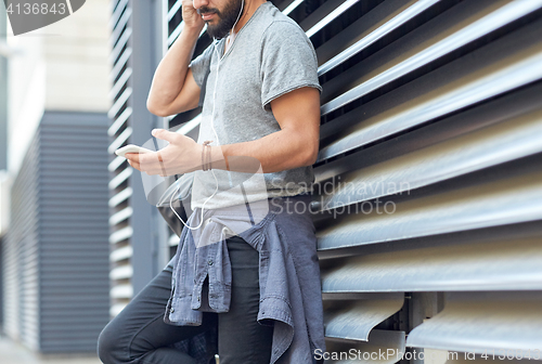 Image of man with earphones, smartphone and bag on street