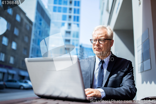 Image of senior businessman with laptop at city street cafe