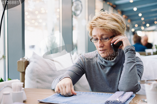 Image of Mid age woman talking on cell phone sitting cafe