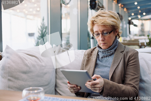 Image of Mid age woman with tablet sitting cafe