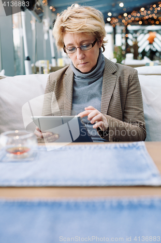 Image of Mid age woman with tablet sitting cafe