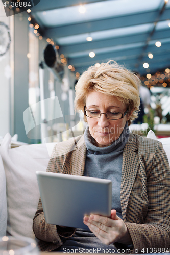 Image of Mid age woman with tablet sitting cafe