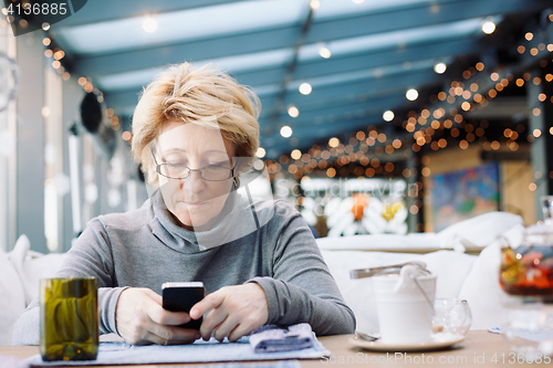Image of Mid age woman with cell phone sitting cafe