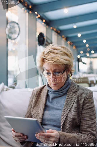 Image of Mid age woman with tablet sitting cafe