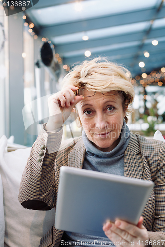 Image of Mid age woman with tablet sitting cafe