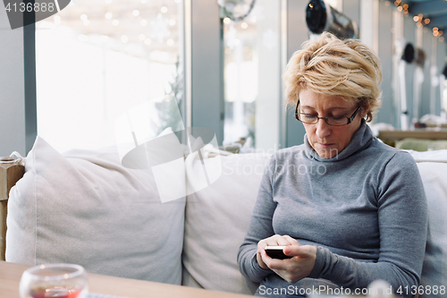 Image of Mid age woman with cell phone sitting cafe