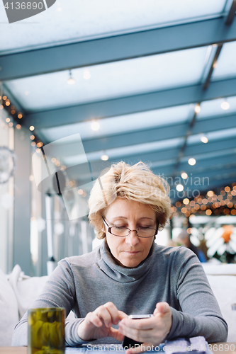 Image of Mid age woman with cell phone sitting cafe