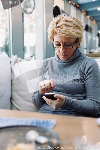 Image of Mid age woman with cell phone sitting cafe