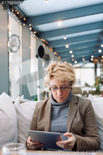 Image of Mid age woman with tablet sitting cafe