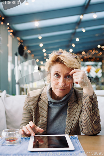 Image of Mid age woman with tablet sitting cafe