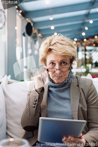 Image of Mid age woman with tablet sitting cafe