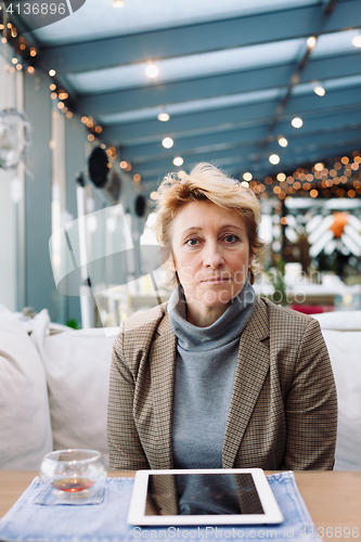 Image of Mid age woman with tablet sitting cafe