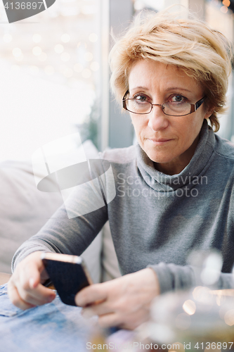 Image of Mid age woman with cell phone sitting cafe