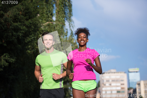 Image of young smiling multiethnic couple jogging in the city