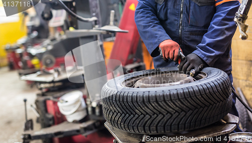 Image of Professional auto mechanic replacing tire on wheel in car repair service.