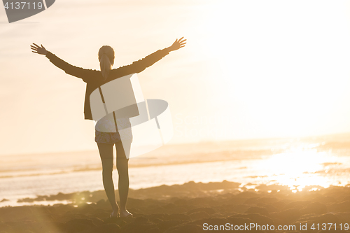 Image of Free woman enjoying freedom on beach at sunset.