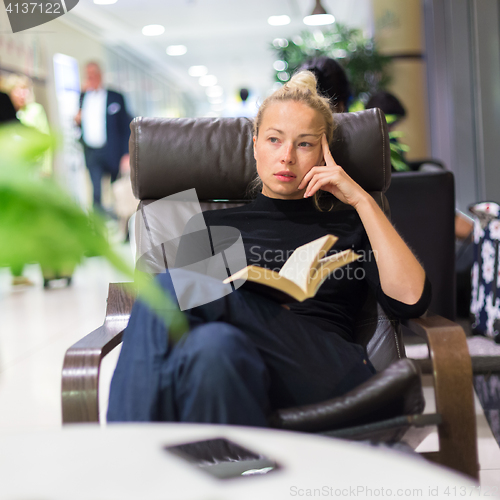 Image of Charming girl sitting by wooden table and reading book