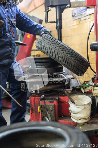 Image of Professional auto mechanic replacing tire on wheel in car repair service.