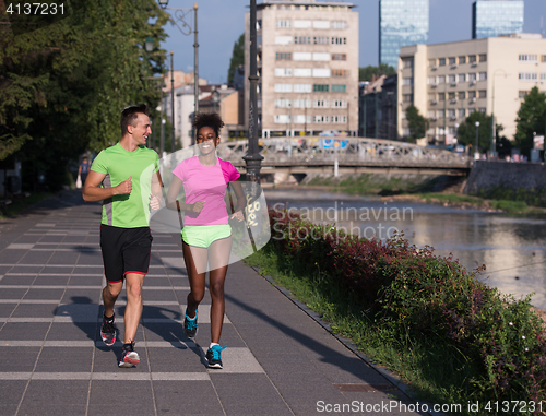 Image of young smiling multiethnic couple jogging in the city