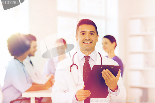 Image of happy doctor with clipboard over medical team
