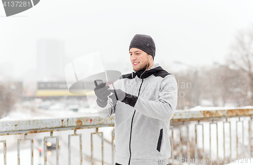 Image of happy man with earphones and smartphone in winter