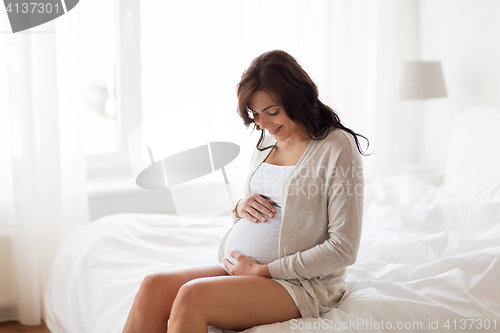 Image of happy pregnant woman sitting on bed at home