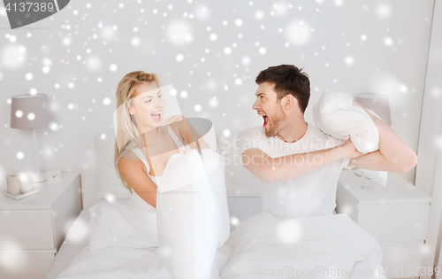 Image of happy couple having pillow fight in bed at home