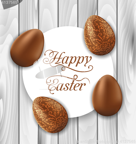 Image of Greeting card with Easter chocolate ornamental eggs on wooden ba