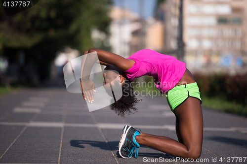 Image of sporty young african american woman stretching outdoors