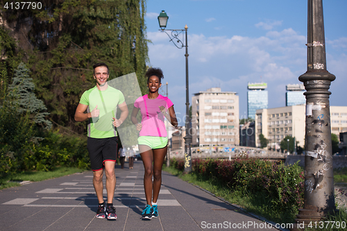Image of young smiling multiethnic couple jogging in the city