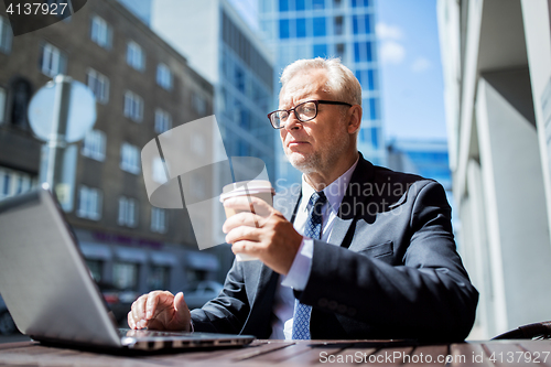 Image of senior businessman with laptop drinking coffee