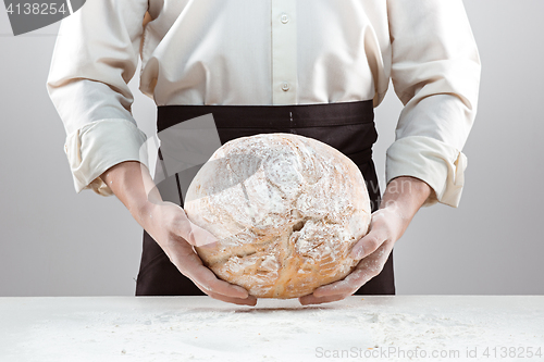 Image of Baker man holding rustic organic loaf of bread in hands