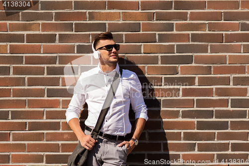 Image of young man in headphones with bag over brickwall