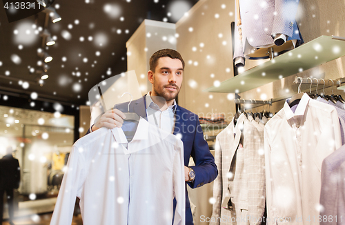 Image of happy young man choosing shirt in clothing store