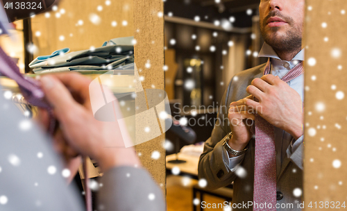 Image of close up of man tying tie at clothing store mirror