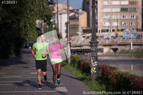 Image of young smiling multiethnic couple jogging in the city