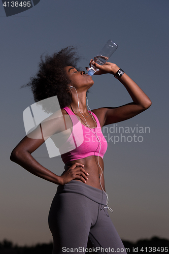 Image of african american woman drinking water after jogging in nature