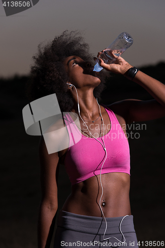 Image of african american woman drinking water after jogging in nature