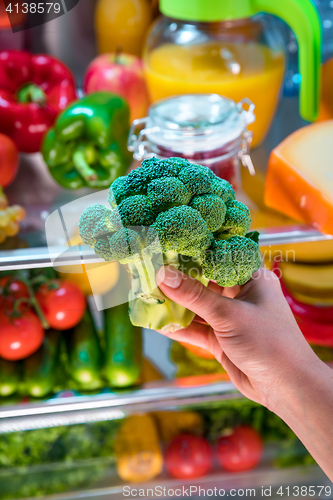 Image of Woman takes the broccoli from the open refrigerator.