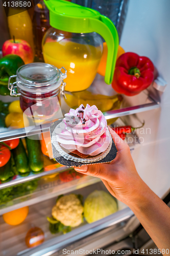 Image of Woman takes the sweet cake from the open refrigerator