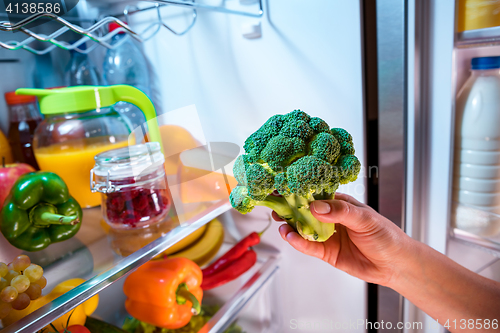 Image of Woman takes the broccoli from the open refrigerator.