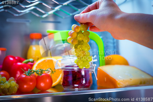 Image of Woman takes the bunch of grapes from the open refrigerator