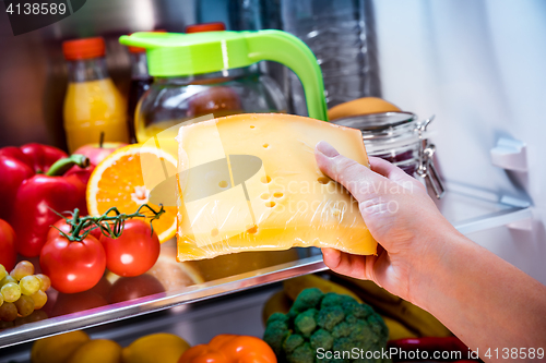 Image of Woman takes the piece of cheese from the open refrigerator