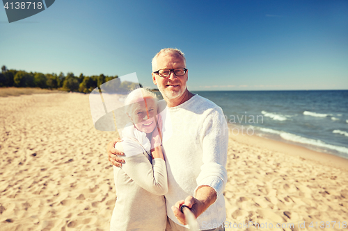 Image of seniors taking picture with selfie stick on beach