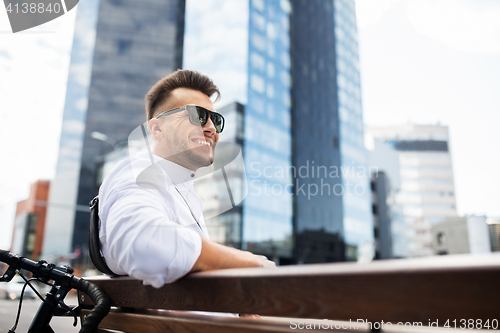 Image of happy young man with bicycle sitting on city bench