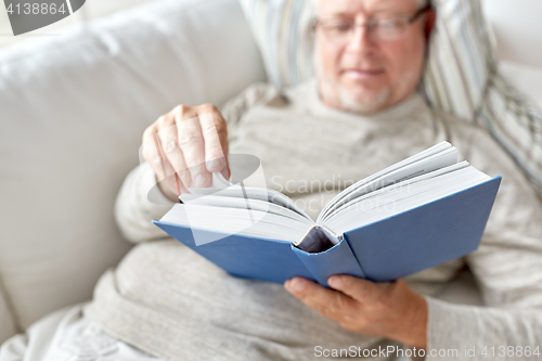 Image of senior man lying on sofa and reading book at home